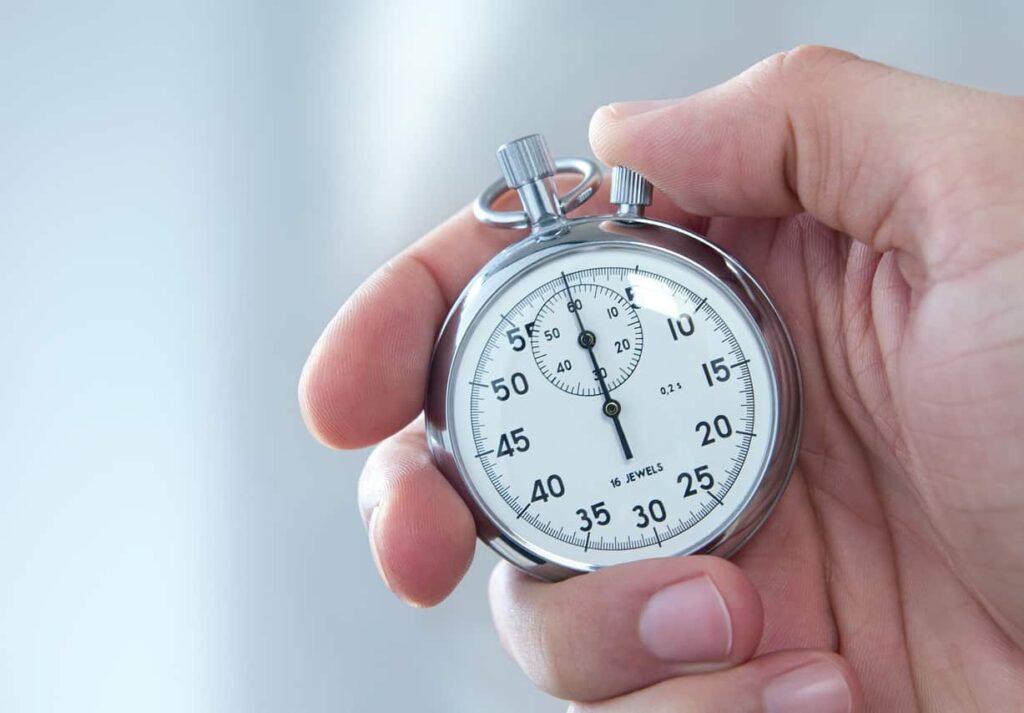 A person holding a silver stopwatch with a white face showing minutes and seconds.