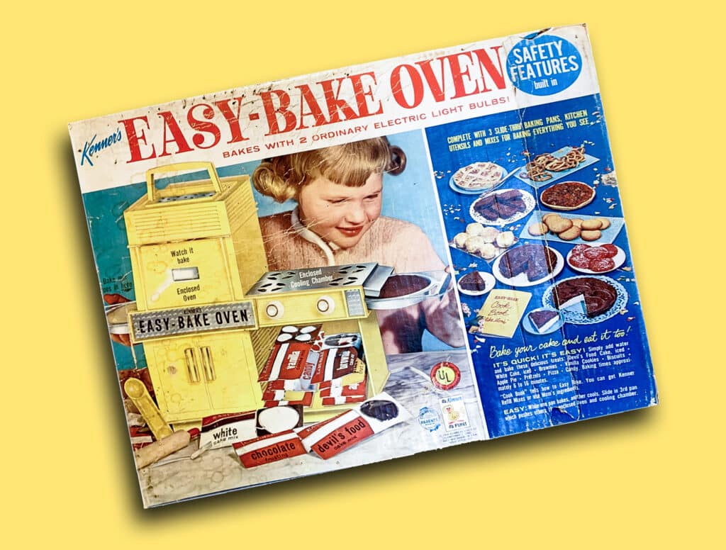 Vintage Easy-Bake Oven box featuring a girl baking, with various baked goods illustrated and safety features noted.