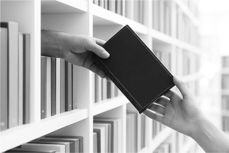 Black and white image of two hands exchanging a book from a bookshelf.