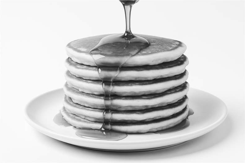 A stack of pancakes on a plate, with syrup pouring over the top and dripping down the sides.