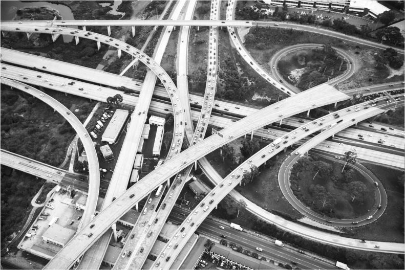 Aerial view of a complex highway interchange with multiple overlapping roads and vehicles in black and white.