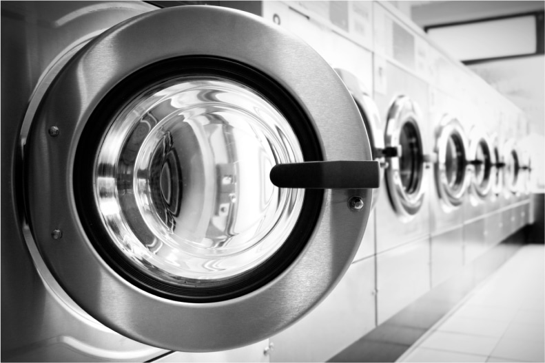 A close-up of a washing machine door handle, with multiple machines visible in the background, in black and white.